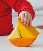 Child holding a Grimms wooden triangular shape from the rolling boats set showing scale