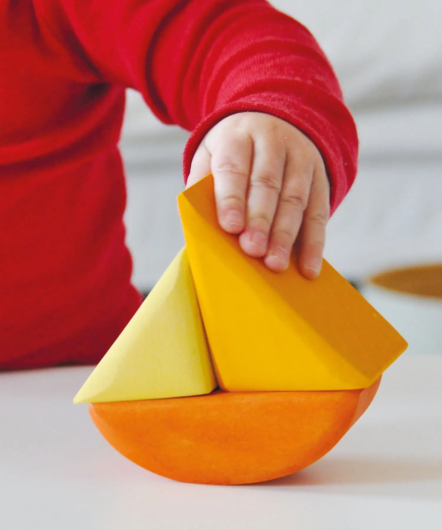 Child holding a Grimms wooden triangular shape from the rolling boats set showing scale