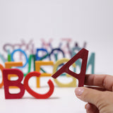 An adult's hand holding up the letter A Grimm's wooden school letter. 