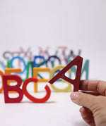An adult's hand holding up the letter A Grimm's wooden school letter. 