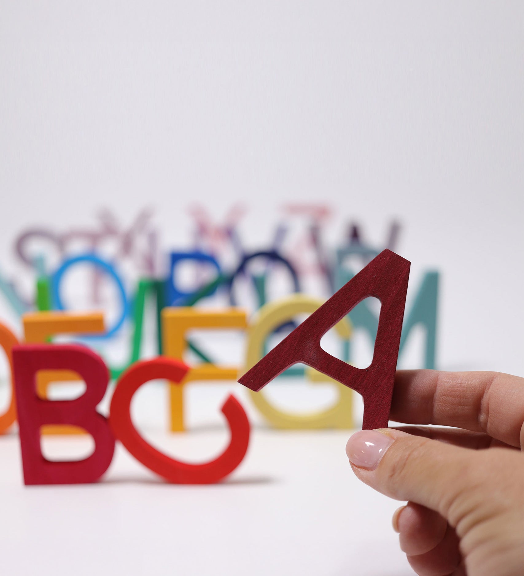 An adult's hand holding up the letter A Grimm's wooden school letter. 