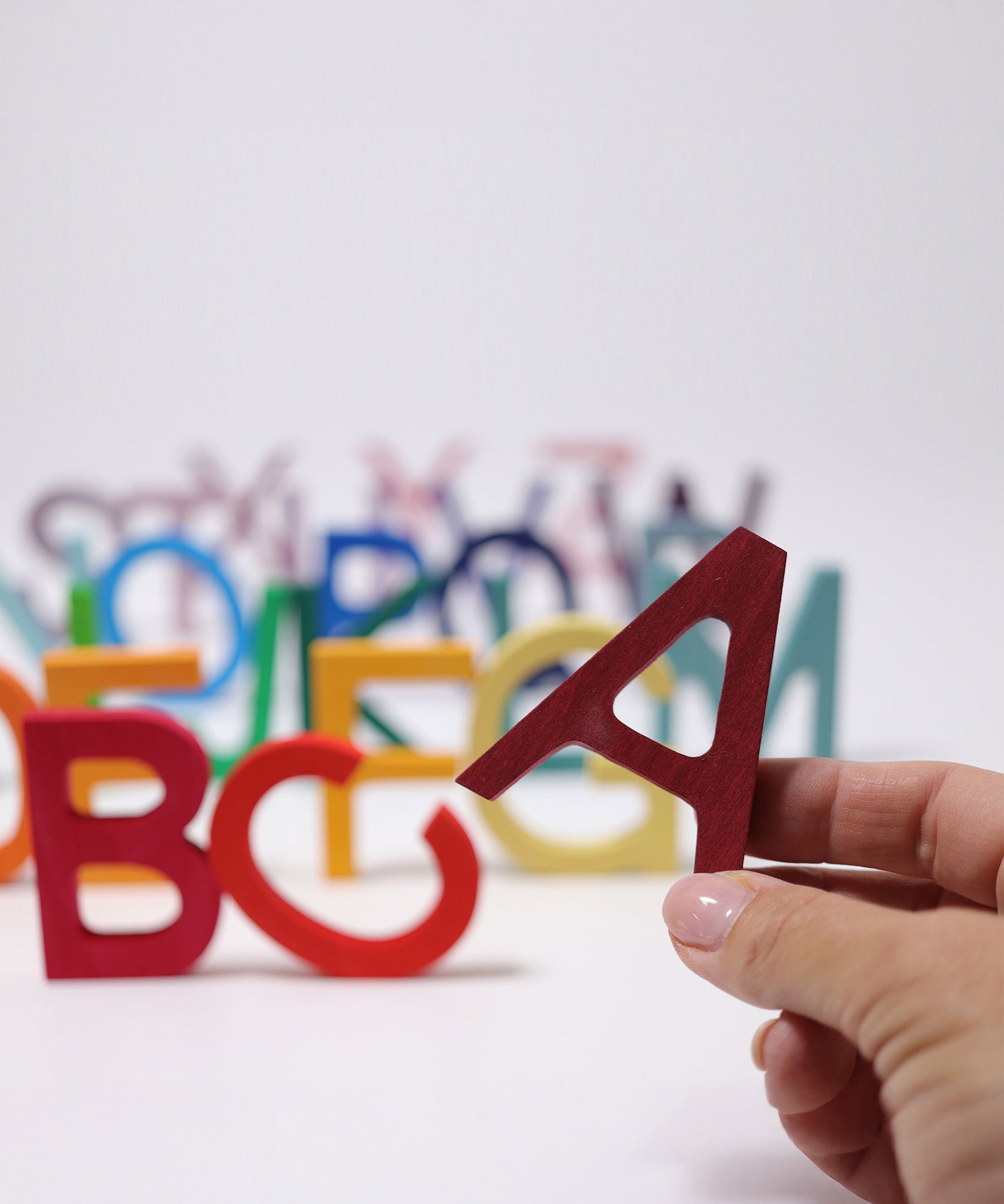An adult's hand holding up the letter A Grimm's wooden school letter. 