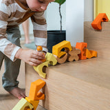 A child playing with the Grimm's Building Set in Yellow, placing them on a wooden step. Wooden blocks in various shades of yellow and natural wood in a yellow coloured wooden storage tray. These Grimm's toys are part of a wide range of wooden toys available here at Babipur. 