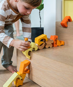 A child playing with the Grimm's Building Set in Yellow, placing them on a wooden step. Wooden blocks in various shades of yellow and natural wood in a yellow coloured wooden storage tray. These Grimm's toys are part of a wide range of wooden toys available here at Babipur. 