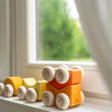 Orange an yellow Grimm's wooden stacking car toy sets placed on a windowsill. These Grimm's toys are part of a wide range of wooden toys available here at Babipur. 