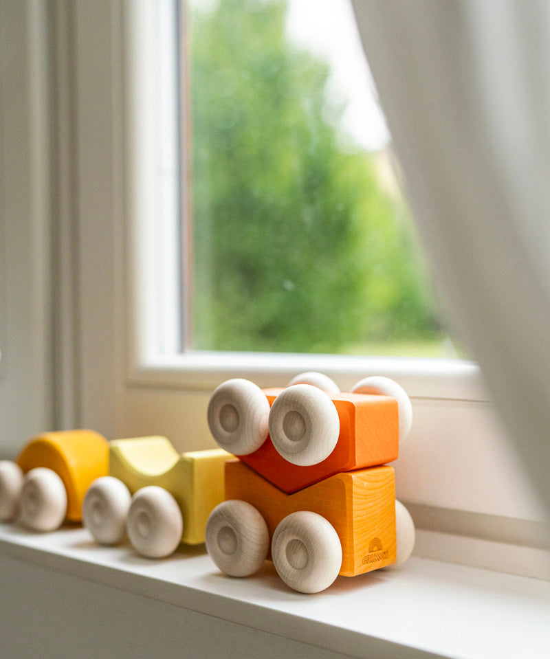 Orange an yellow Grimm's wooden stacking car toy sets placed on a windowsill. These Grimm's toys are part of a wide range of wooden toys available here at Babipur. 