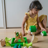 A child hand playing with the Grimm's green squirrel Building Set and green stacking cars. Wooden blocks in various shades of green and natural wood in a green coloured wooden storage tray. These Grimm's toys are part of a wide range of wooden toys available here at Babipur. 