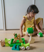 A child hand playing with the Grimm's green squirrel Building Set and green stacking cars. Wooden blocks in various shades of green and natural wood in a green coloured wooden storage tray. These Grimm's toys are part of a wide range of wooden toys available here at Babipur. 