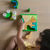 An overhead view of a child playing with the Grimm's green squirrel Building Set. Wooden blocks in various shades of green and natural wood in a green coloured wooden storage tray. These Grimm's toys are part of a wide range of wooden toys available here at Babipur. 