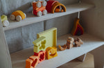 The blocks from the Grimm's yellow building set placed on a shelf with the yellow tray behind them. These Grimm's toys are part of a wide range of wooden toys available here at Babipur. 
