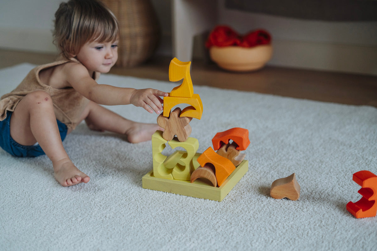 A child playing with the yellow and natural wooden blocks from the Grimm's yellow building set. The child is stacking them on top of each other on the yellow coloured storage tray that they come with. These Grimm's toys are part of a wide range of wooden toys available here at Babipur. 