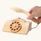 Grimm's wooden toy telephone. Adult's hand can be seen lifting the receiver off the base. 