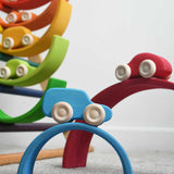 The cars from the Grimm's 6 Coloured Wooden Cars set placed on matching coloured pieces from the large Grimm's rainbow tunnel. The blue car can be seen at the front balanced on the blue coloured rainbow arch. These wooden toy cars are part of a wide range of Grimm's wooden toys available here at Babipur.
