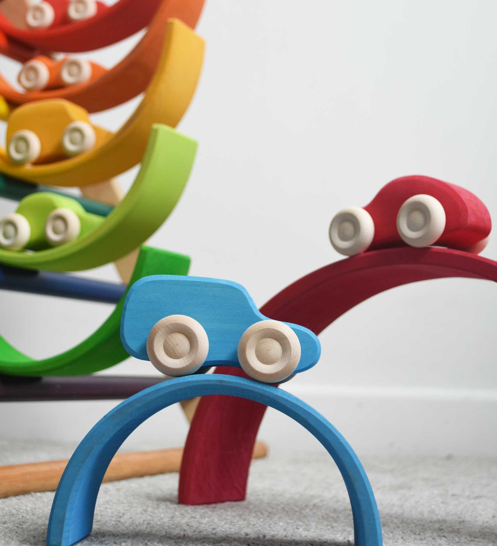 The cars from the Grimm's 6 Coloured Wooden Cars set placed on matching coloured pieces from the large Grimm's rainbow tunnel. The blue car can be seen at the front balanced on the blue coloured rainbow arch. These wooden toy cars are part of a wide range of Grimm's wooden toys available here at Babipur.
