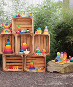 A display of different Grimms stacking and wooden toys standing inside crates in a garden