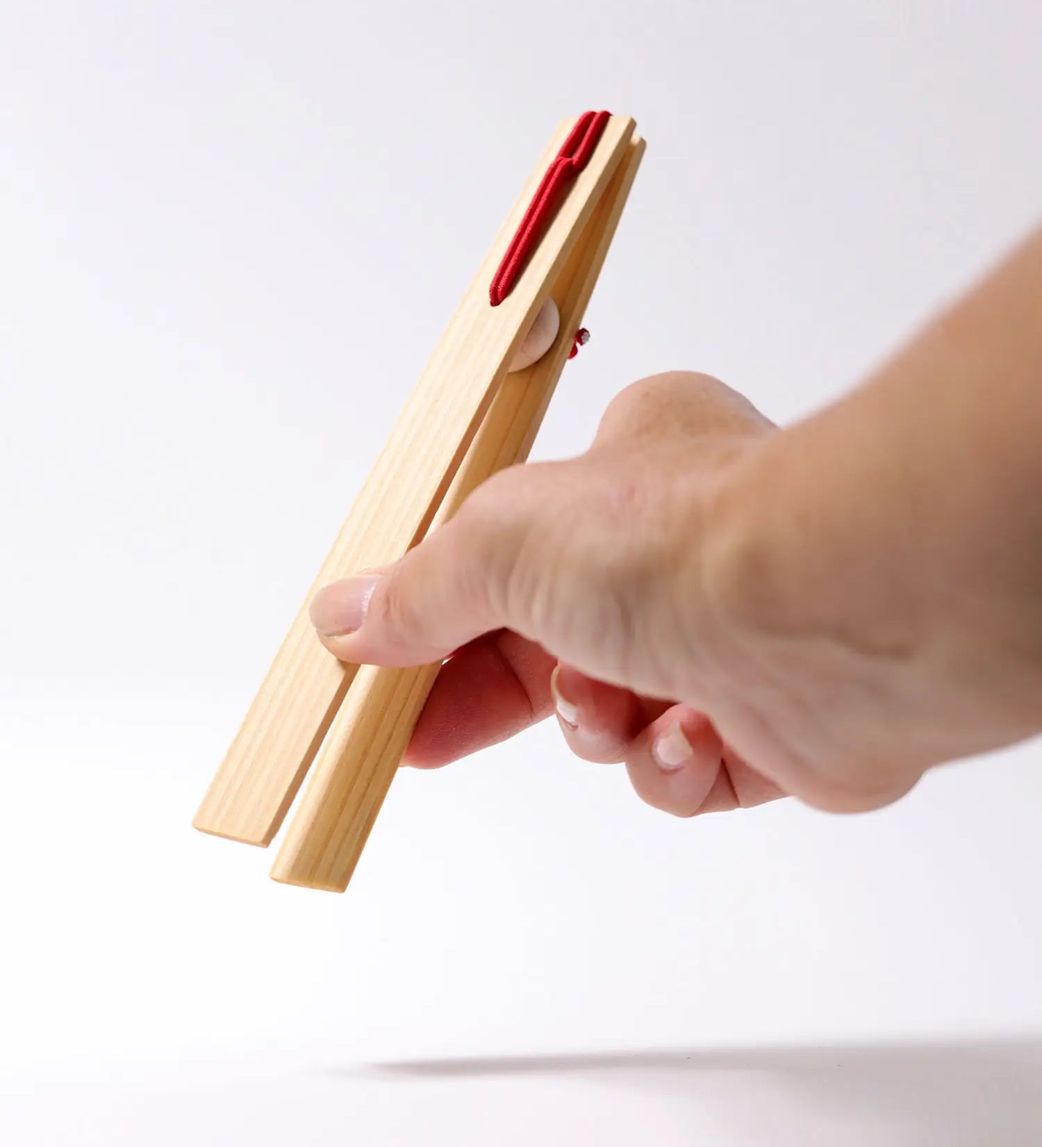 Adult hand holding the Grimms wooden 18cm tweezers  showing scale