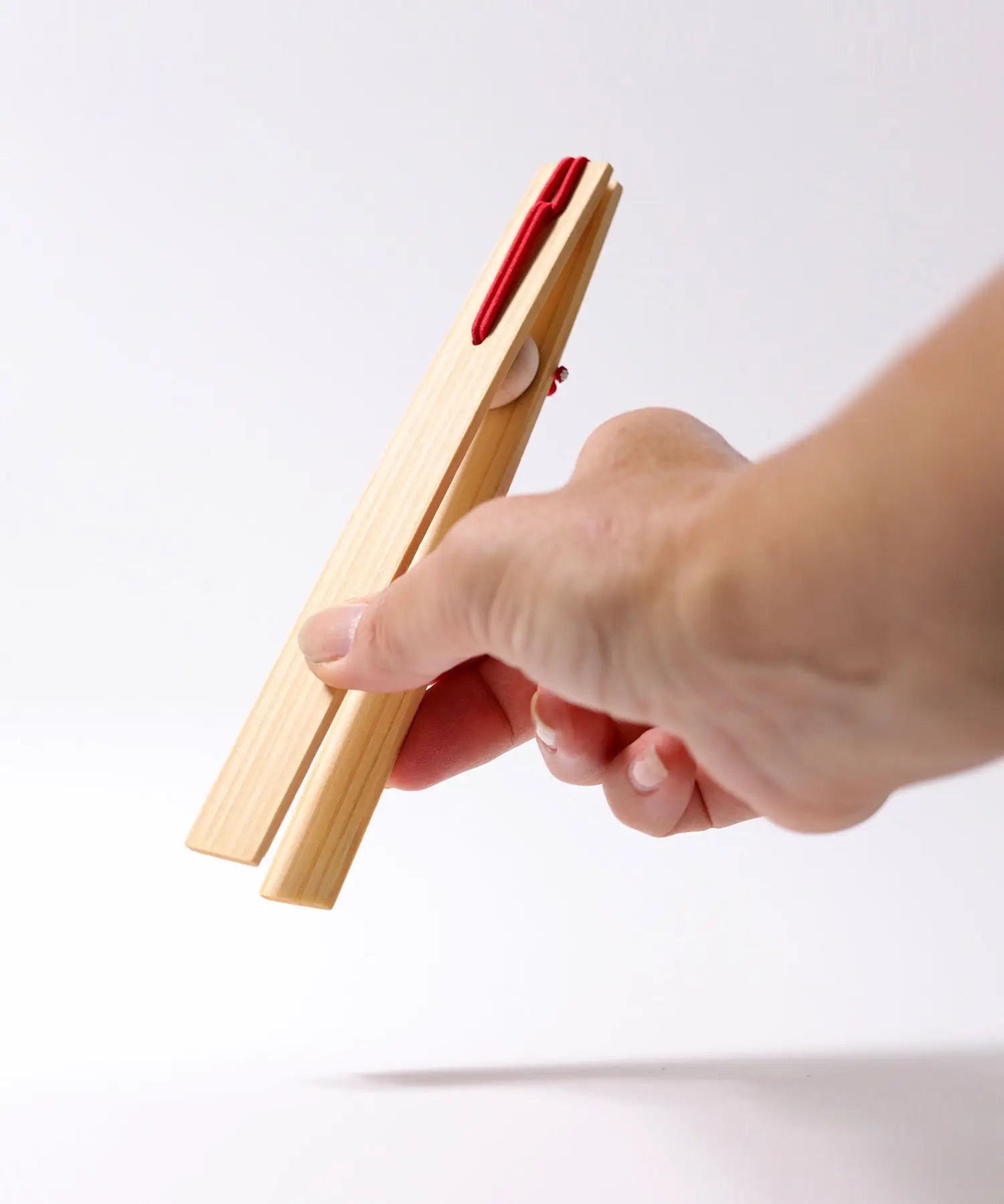 Adult hand holding the Grimms wooden 18cm tweezers  showing scale