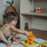 A child playing with the yellow and natural wooden blocks from the Grimm's yellow building set. The child is stacking them on top of each other on the yellow coloured storage tray that they come with. These Grimm's toys are part of a wide range of wooden toys available here at Babipur. 