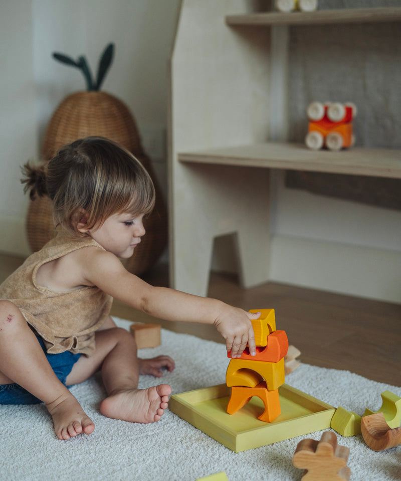 A child playing with the yellow and natural wooden blocks from the Grimm's yellow building set. The child is stacking them on top of each other on the yellow coloured storage tray that they come with. These Grimm's toys are part of a wide range of wooden toys available here at Babipur. 