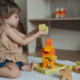 A child playing with the yellow and natural wooden blocks from the Grimm's yellow building set. The child is stacking them on top of each other on the yellow coloured storage tray that they come with. These Grimm's toys are part of a wide range of wooden toys available here at Babipur. 