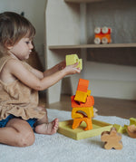 A child playing with the yellow and natural wooden blocks from the Grimm's yellow building set. The child is stacking them on top of each other on the yellow coloured storage tray that they come with. These Grimm's toys are part of a wide range of wooden toys available here at Babipur. 