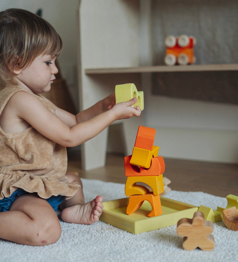 A child playing with the yellow and natural wooden blocks from the Grimm's yellow building set. The child is stacking them on top of each other on the yellow coloured storage tray that they come with. These Grimm's toys are part of a wide range of wooden toys available here at Babipur. 