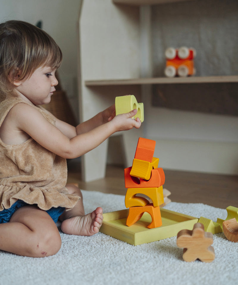 A child playing with the yellow and natural wooden blocks from the Grimm's yellow building set. The child is stacking them on top of each other on the yellow coloured storage tray that they come with. These Grimm's toys are part of a wide range of wooden toys available here at Babipur. 