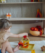 A child playing with the yellow and natural wooden blocks from the Grimm's yellow building set. The child is stacking them on top of each other on the yellow coloured storage tray that they come with. These Grimm's toys are part of a wide range of wooden toys available here at Babipur. 