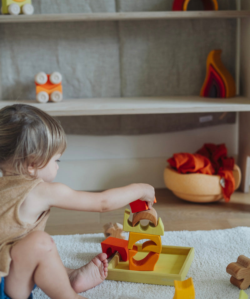 A child playing with the yellow and natural wooden blocks from the Grimm's yellow building set. The child is stacking them on top of each other on the yellow coloured storage tray that they come with. These Grimm's toys are part of a wide range of wooden toys available here at Babipur. 