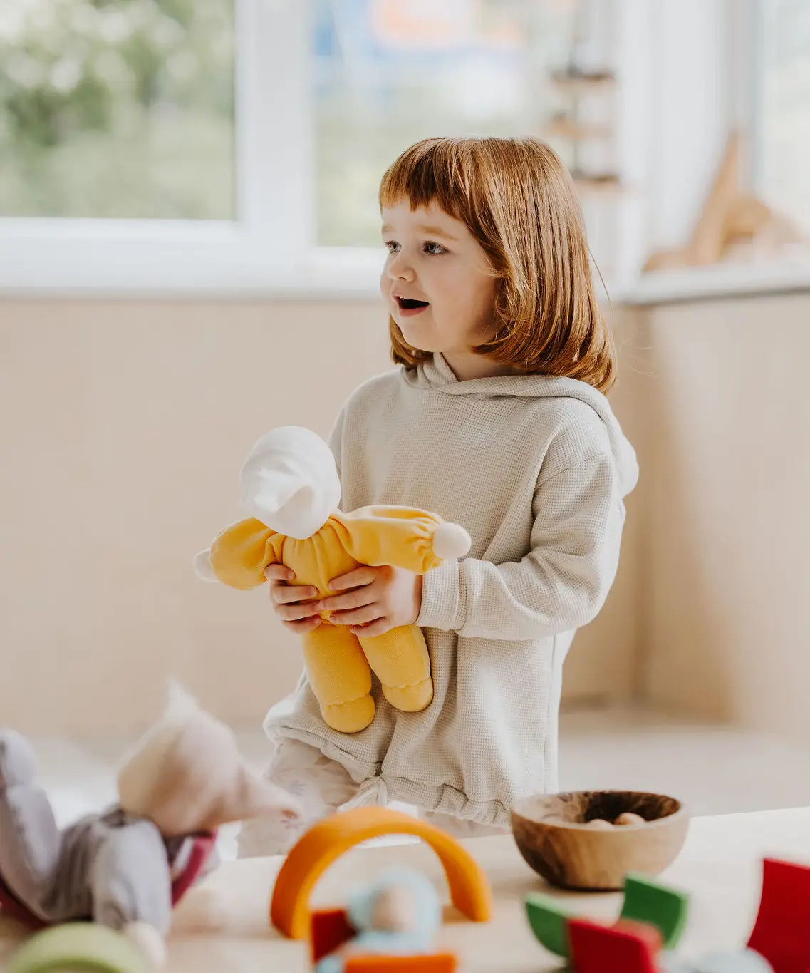 Child holding a Grimms yellow soft Waldorf doll showing size