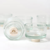 The Grimm's set of glass tealight holder, one shows the bottom with a base plug with a Grimm's logoto lift if off the surface
