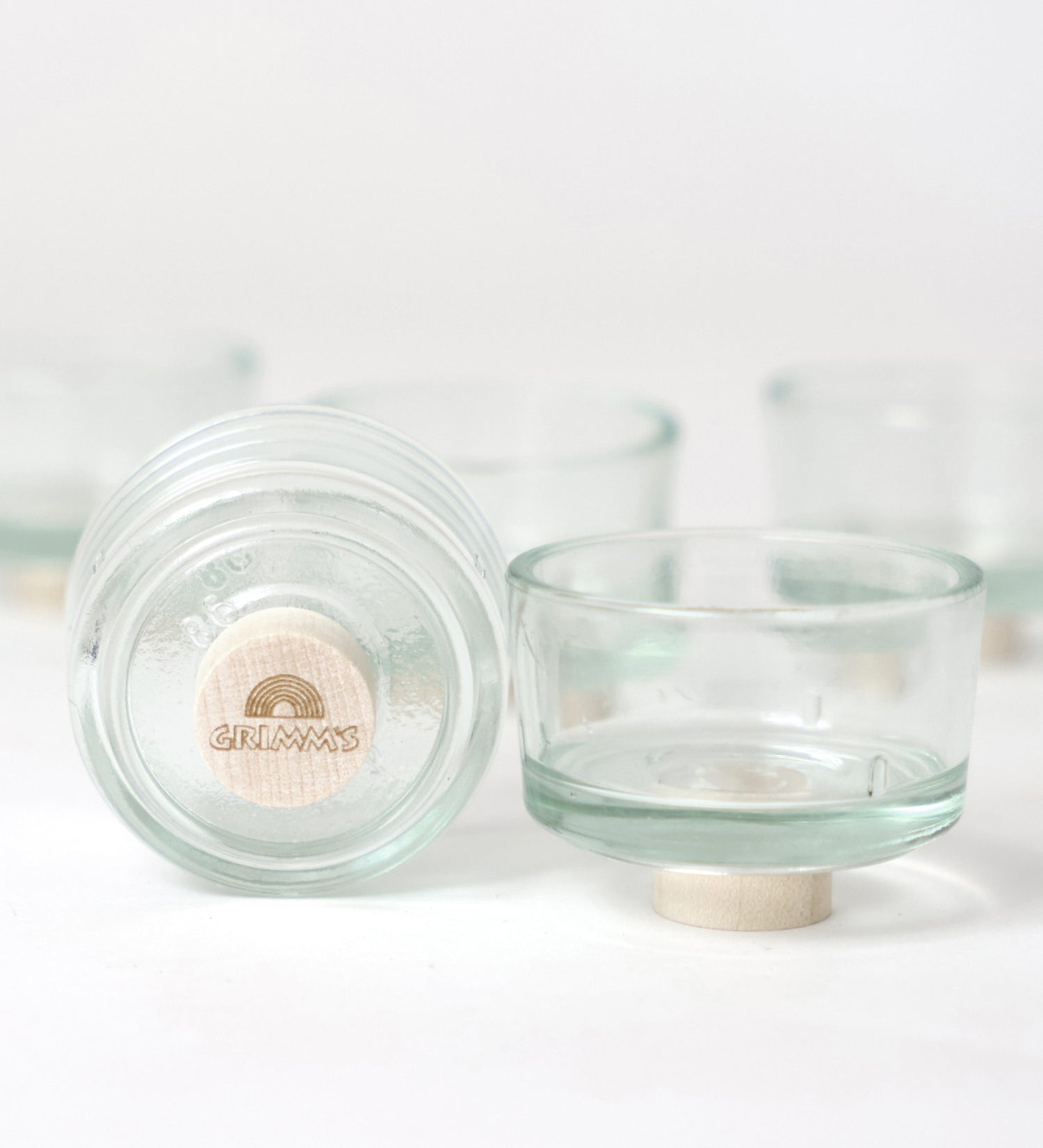 The Grimm's set of glass tealight holder, one shows the bottom with a base plug with a Grimm's logoto lift if off the surface