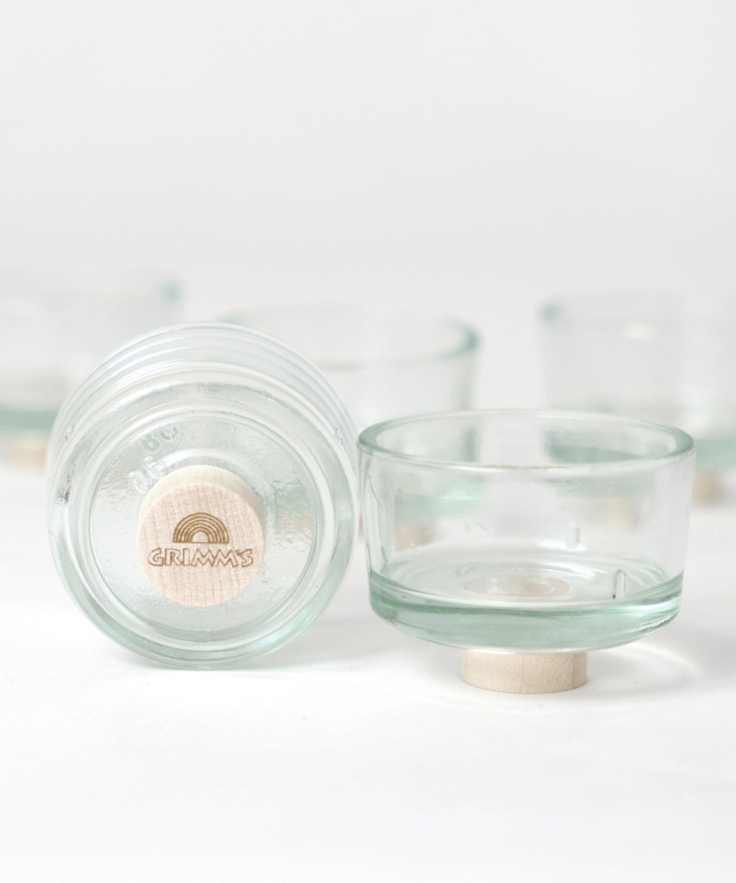 The Grimm's set of glass tealight holder, one shows the bottom with a base plug with a Grimm's logoto lift if off the surface