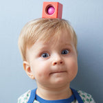 A red wooden block from the Haba blocks with sounds set on top of a child's head