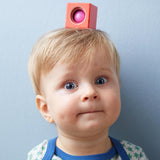 A red wooden block from the Haba blocks with sounds set on top of a child's head