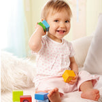 A child sitting with the blue and green wooden block from the Haba blocks with sounds set next to their ear
