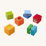 Green, orange, blue and red wooden cubes from the Haba blocks with sounds set on a cream background.