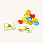 Red, yellow, green and orange wooden elephants from the Haba elephant stacking game stacked on top of each other with challenge card on a cream background. 
