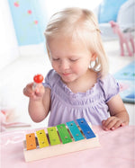  Xylophone Toy Instrument. A wooden drumming stick on top of a row of colourful flat metal bars pinned into a wooden base with each one being a different musical note