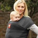 Woman carrying baby in the charcoal Hana baby carrier in front of a grey background