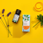 Harmony pure essential oil blend in a blue glass bottle next to a decorative blue cardboard box, with lavender flowers, orange peel and geranium leaf on a yellow background. 