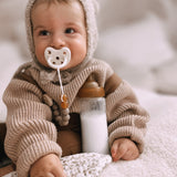 Close up of baby sat with a bottle of milk and a dummy in their mouth