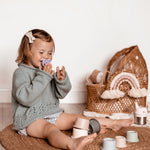Girl sat on the floor laughing with a Hevea orthodontic pacifier in her mouth