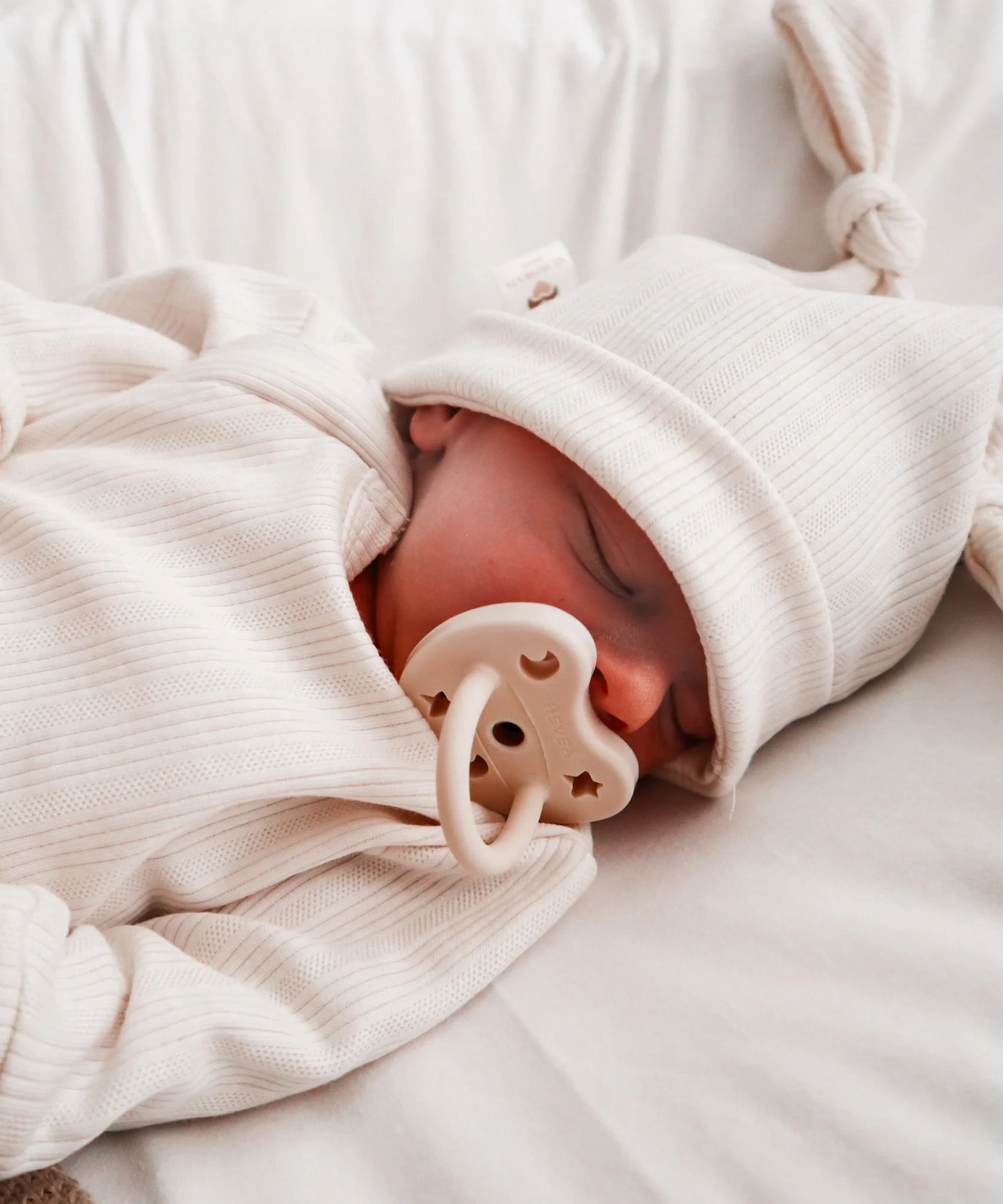 A sleeping baby with The Hevea natural rubber pacifier dummy with a symmetrical nipple shape, in milky white 