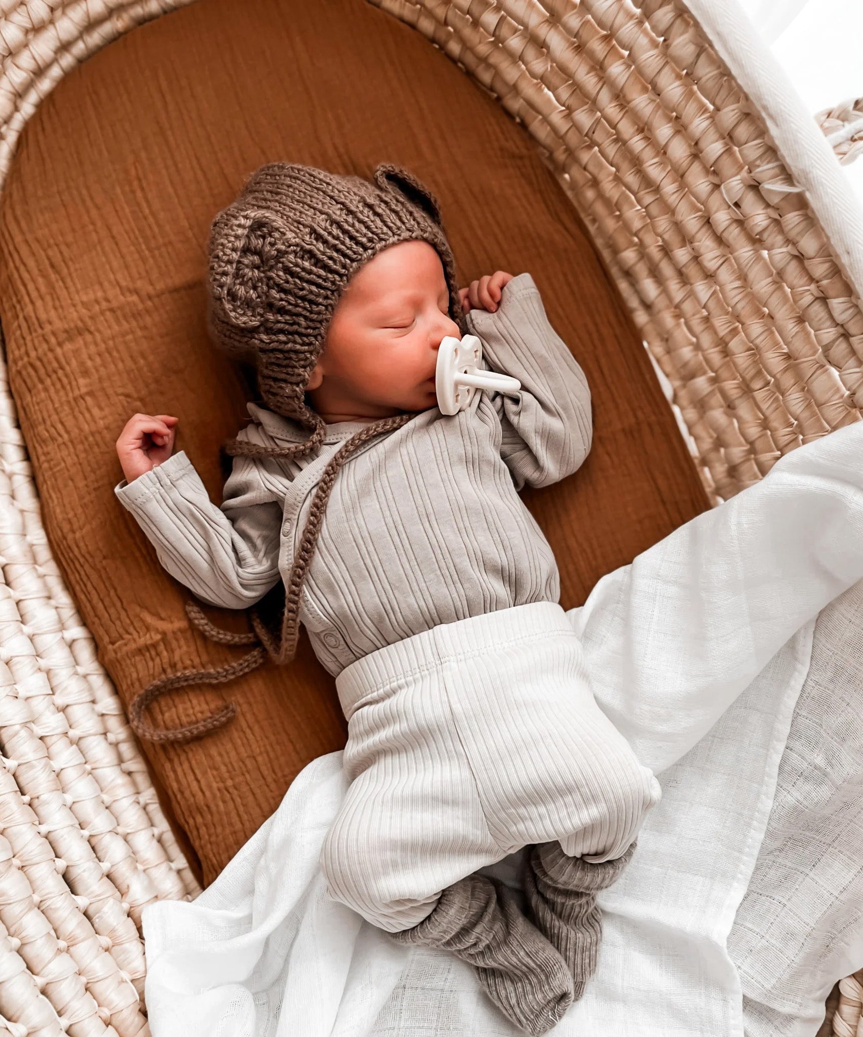 A sleeping baby in a crib with The Hevea natural rubber pacifier dummy with a symmetrical nipple shape in its mouth, in milky white colour 