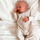 A very young baby with a Hevea natural rubber pacifier dummy with a symmetrical nipple shape, in a natural orange colour.