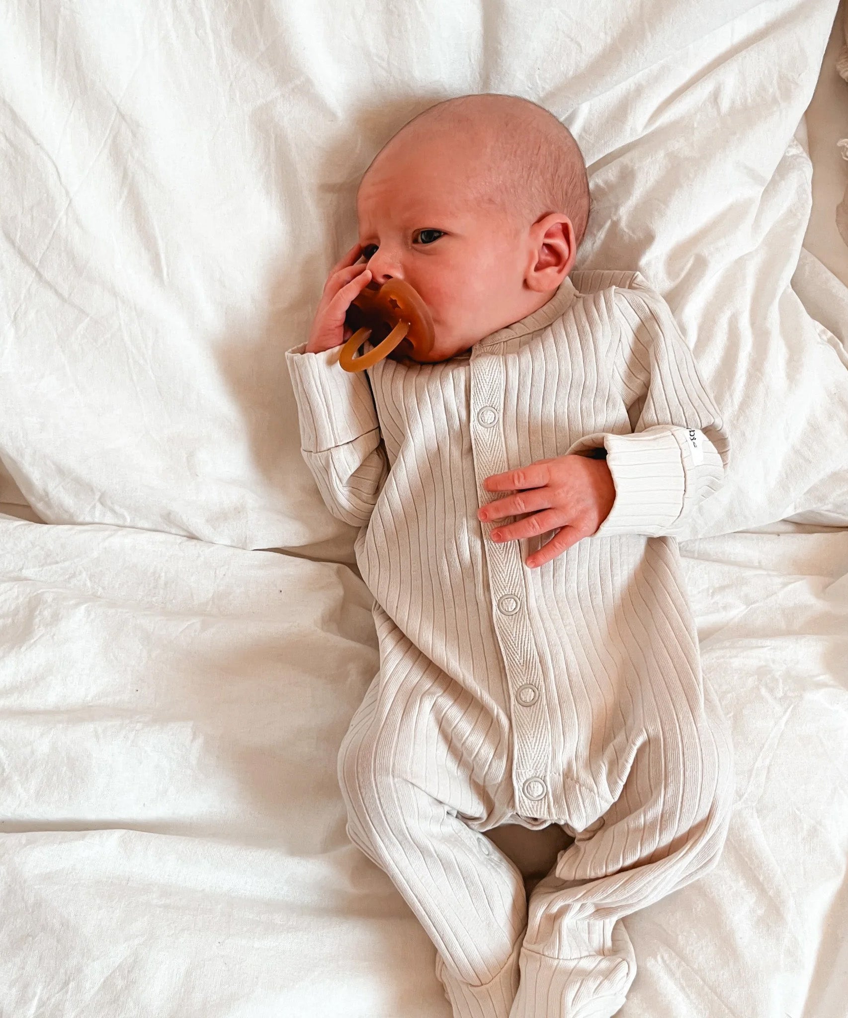 A very young baby with a Hevea natural rubber pacifier dummy with a symmetrical nipple shape, in a natural orange colour.