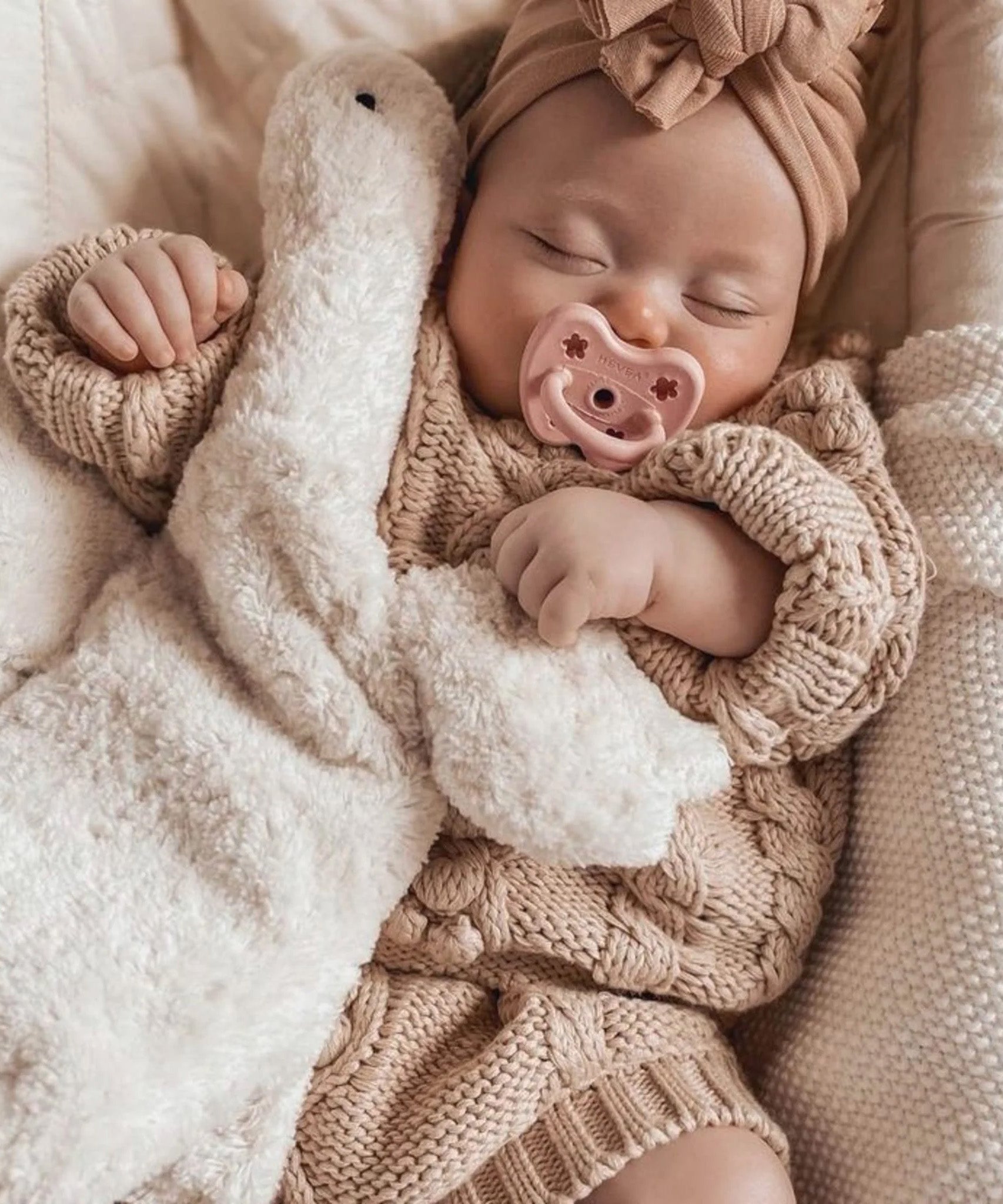 A baby sleeping with a Senger stuffed toy, with a Hevea natural rubber pacifier in pink
