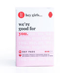 Hey Girls Natural Bamboo & Corn Fibre Disposable Day Pad open in someone's hand on a pink and red background