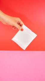 Hey Girls Natural Bamboo & Corn Fibre Disposable Day Pad wrapped in packaging held in someone's hand in front of a red and pink background